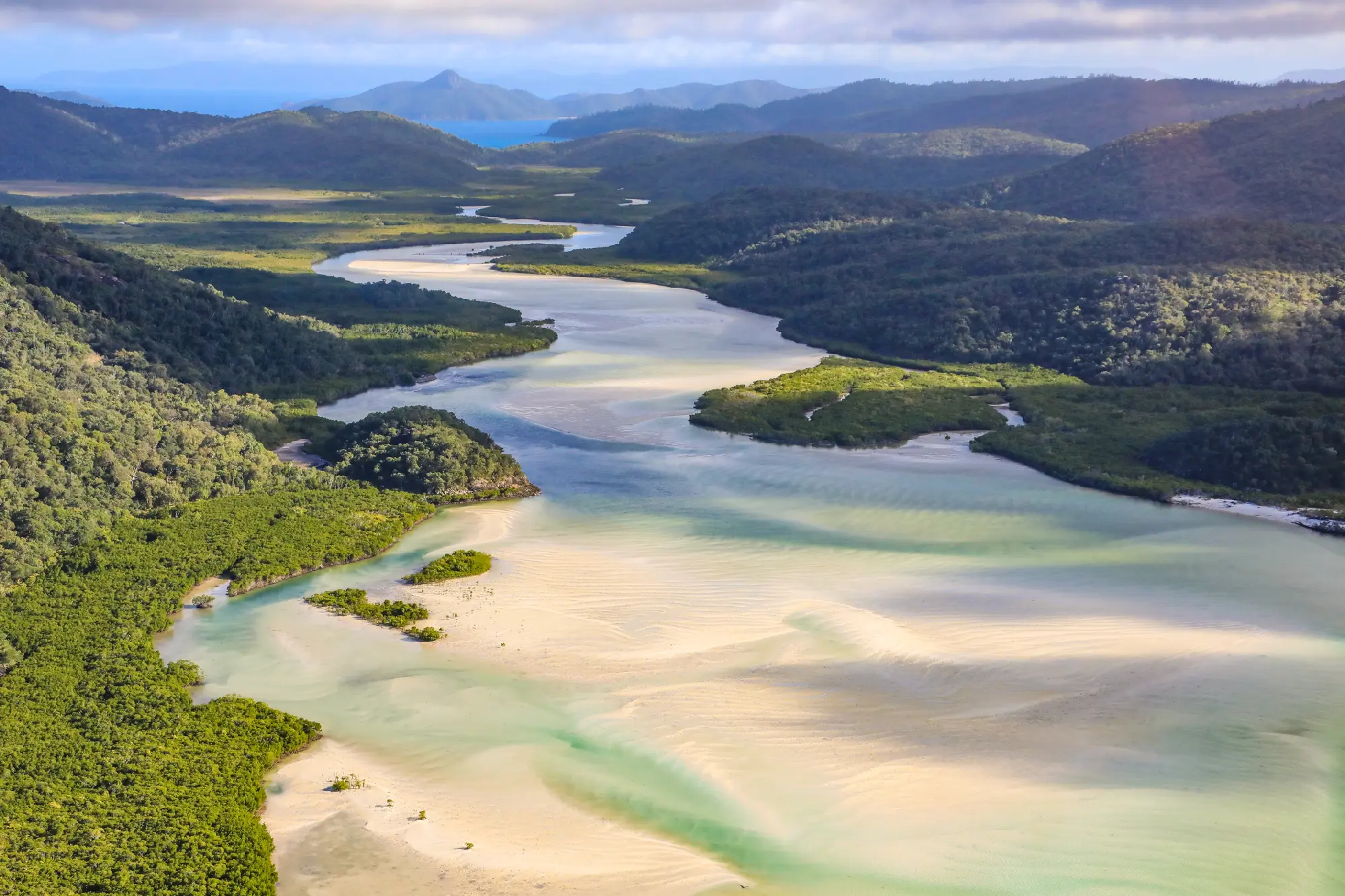 Aerial view of Hill Inlet with winding turquoise channels, pale sandbanks and forested hills on Whitsunday Island, Queensland.