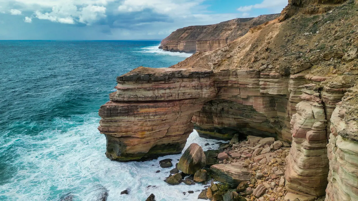 Natural Bridge sea arch surrounded by layered sandstone cliffs and breaking ocean waves in Kalbarri National Park.