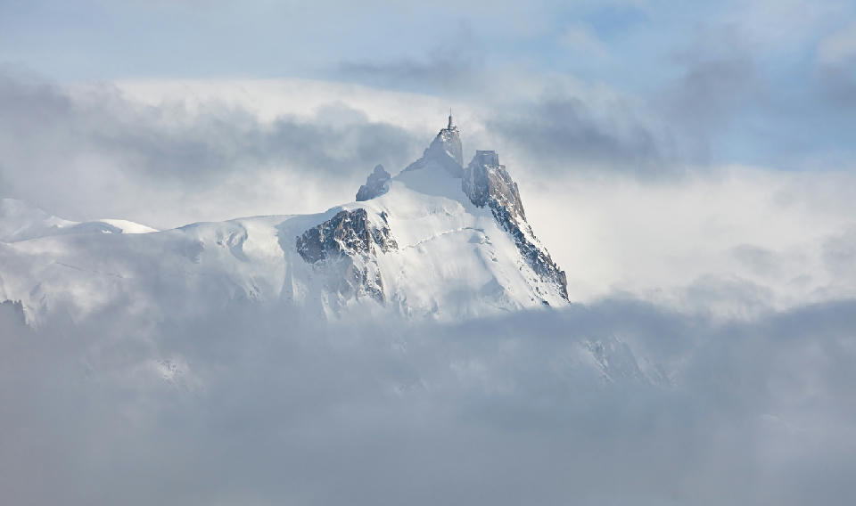 Aiguille du Midi peak emerging through clouds in the Mont Blanc Massif with snow-covered slopes.