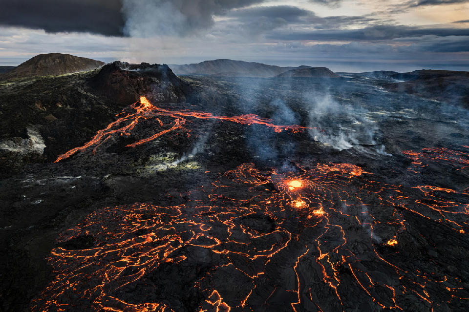 Drone view of glowing lava streams and cooling black crust at Fagradalsfjall volcano, Reykjanes Peninsula, Iceland.