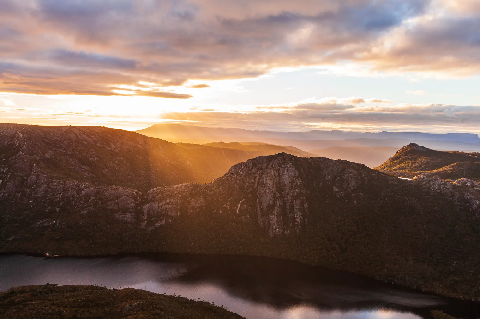 Golden morning light over rugged mountains and an alpine lake in Cradle Mountain–Lake St Clair National Park, Tasmania.