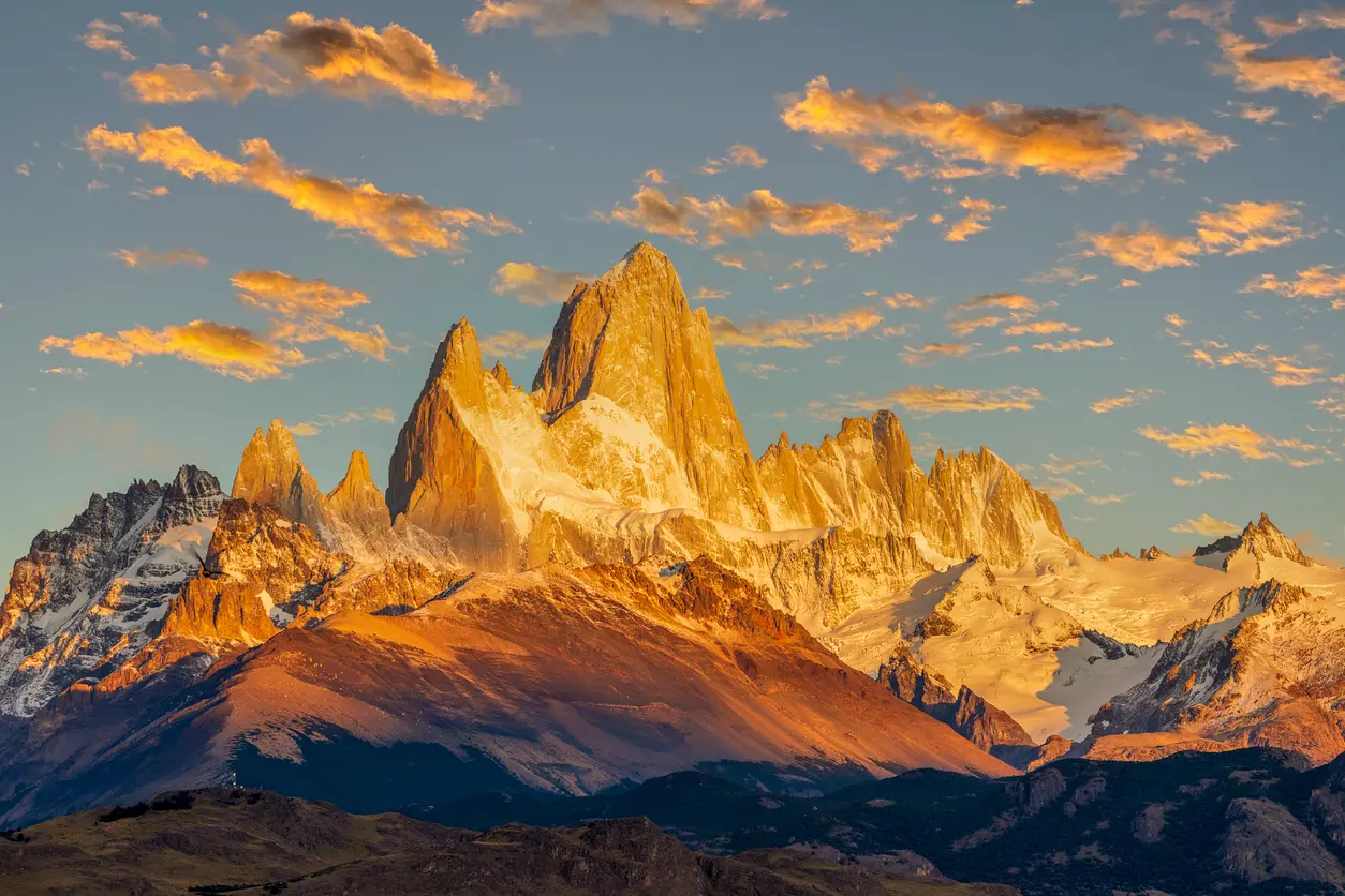 Mount Fitz Roy glowing orange at sunrise with dramatic clouds in Patagonia, Argentina.