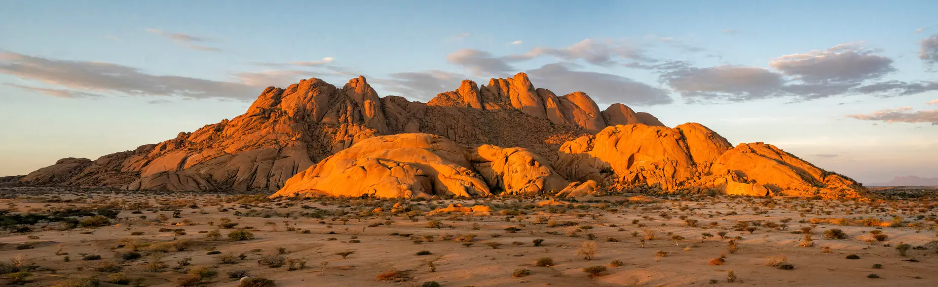 Panoramic view of granite peaks and desert plains at Spitzkoppe in Namibia under warm evening light.