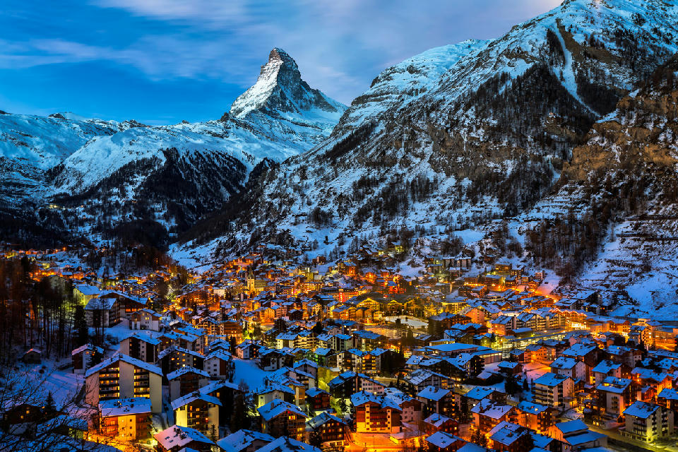 Evening view of Zermatt village with illuminated chalets beneath the Matterhorn in winter, Switzerland.