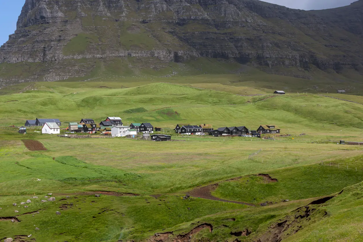 Wide view of Gásadalur village with traditional houses surrounded by grassland and mountains on Vágar Island, Faroe Islands.