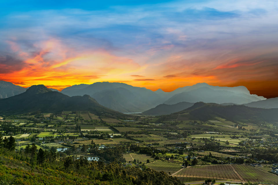 Golden sunset above Franschhoek Valley viewed from Franschhoek Pass with vineyards, mountain ridges, and dramatic evening skies in the Western Cape.