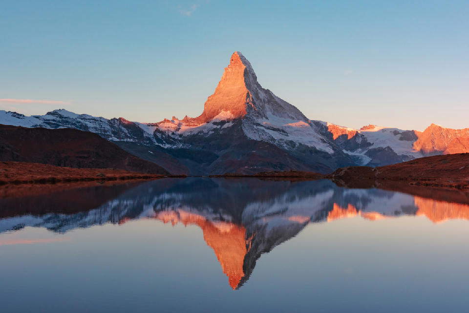 Matterhorn peak illuminated by sunrise and reflected in Stellisee lake near Zermatt, Switzerland, with calm water and clear sky.