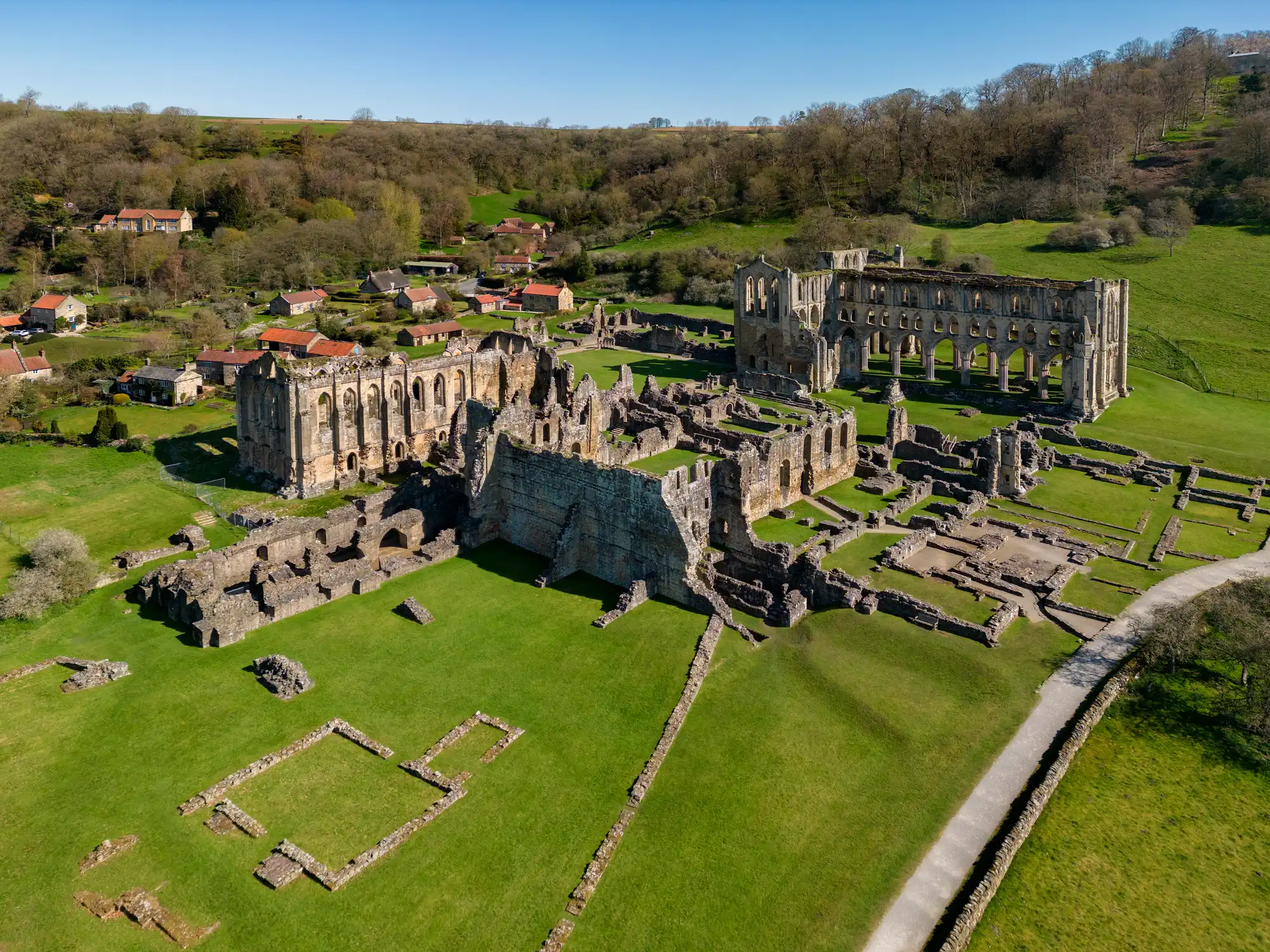 Wide aerial view of Rievaulx Abbey showing the complete Cistercian monastery ruins, Gothic church walls and surrounding green valley in North Yorkshire.