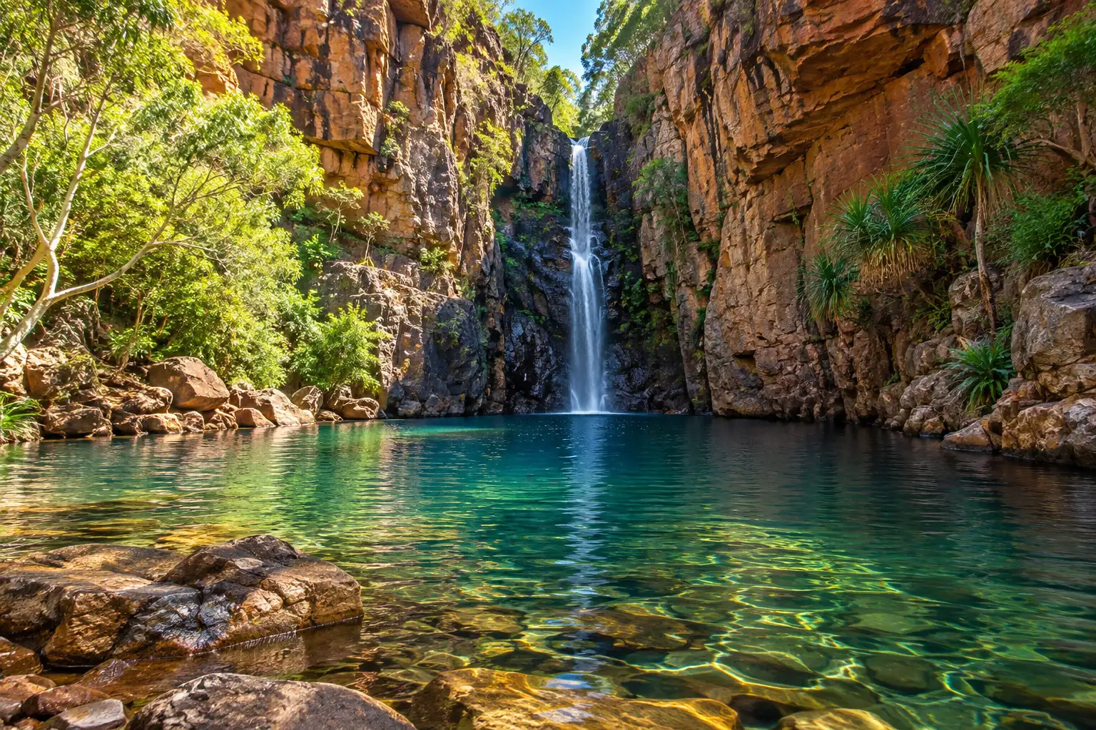 Waterfall cascading between towering red sandstone cliffs into the clear emerald pool at Emma Gorge.