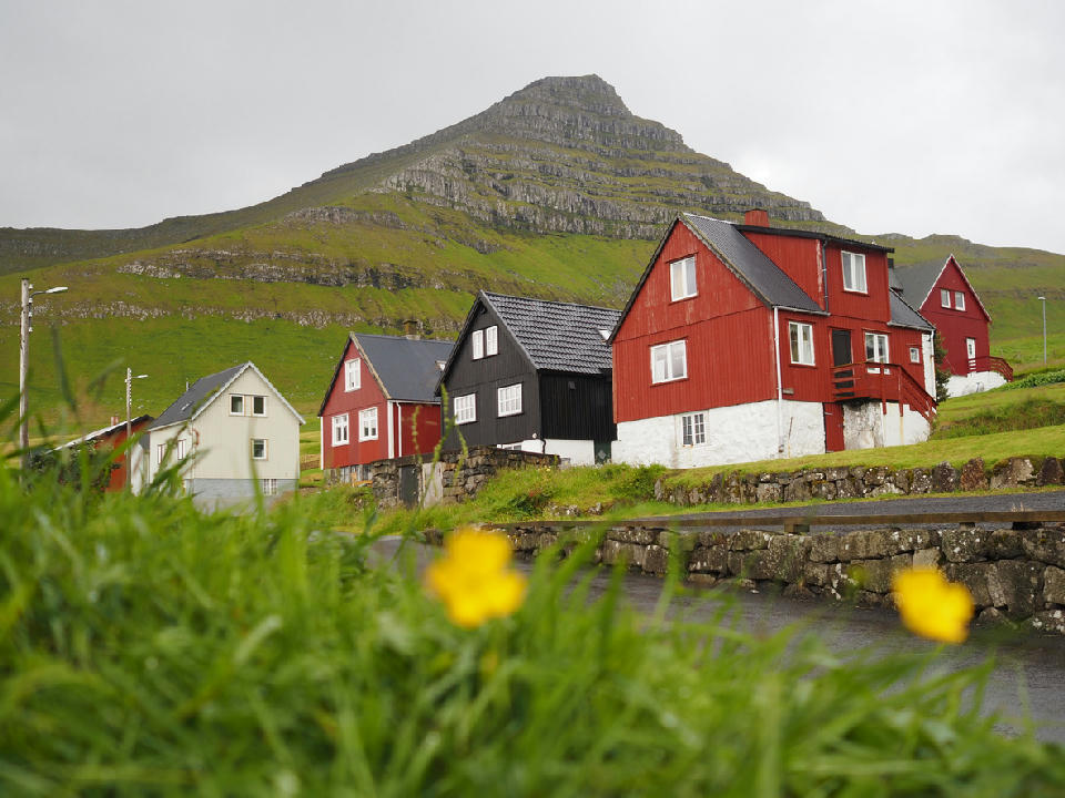 Colorful wooden houses in Mikladalur village beneath a stepped basalt mountain on Kalsoy, Faroe Islands.