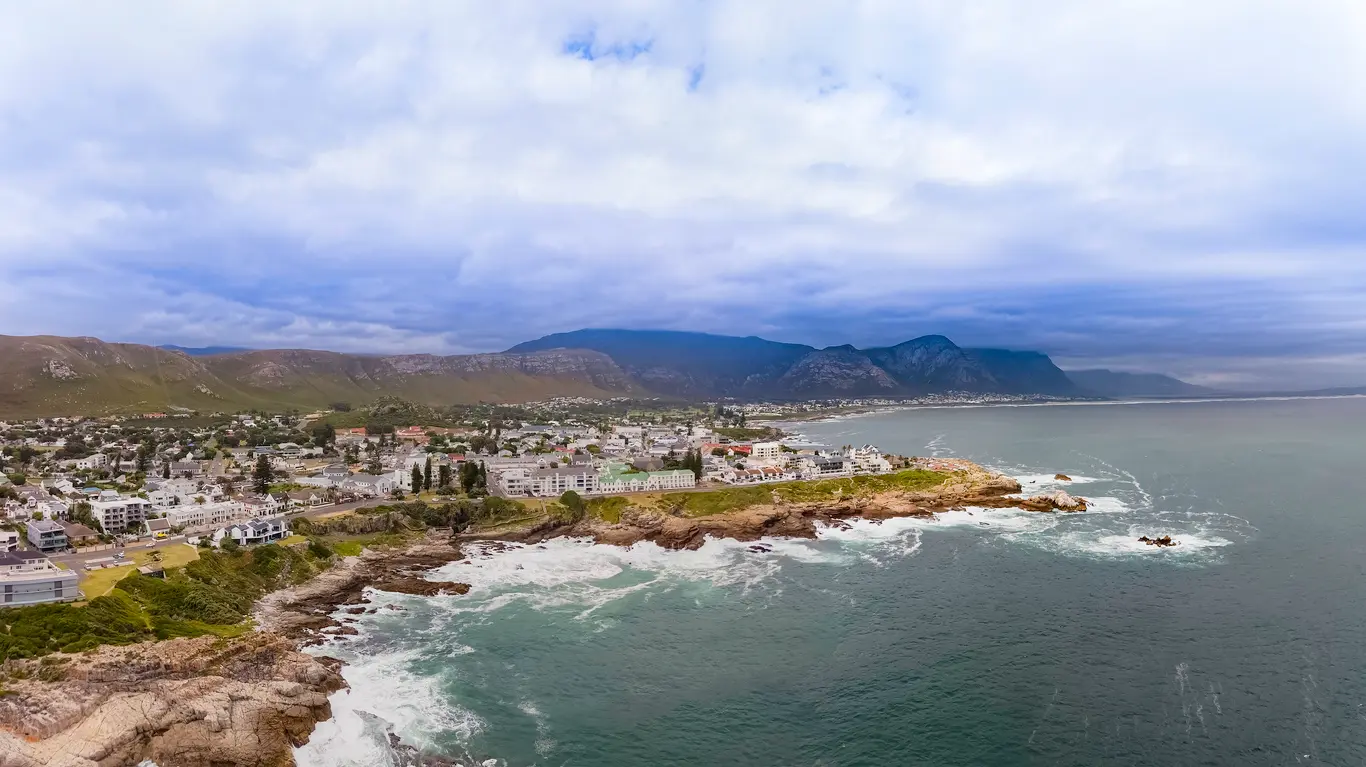 Coastal aerial panorama of Hermanus with rocky shoreline, ocean cliffs, and mountains along the Whale Coast in South Africa.