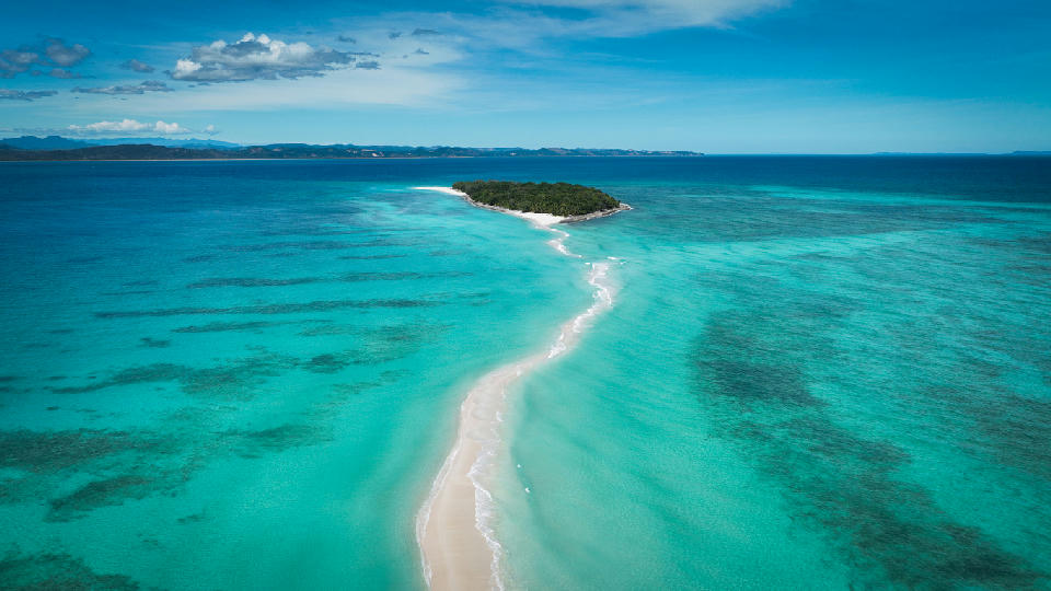 Drone view of the Nosy Iranja sandbar in Madagascar with white sand, shallow turquoise water, reef textures, and tropical islands in the Indian Ocean.