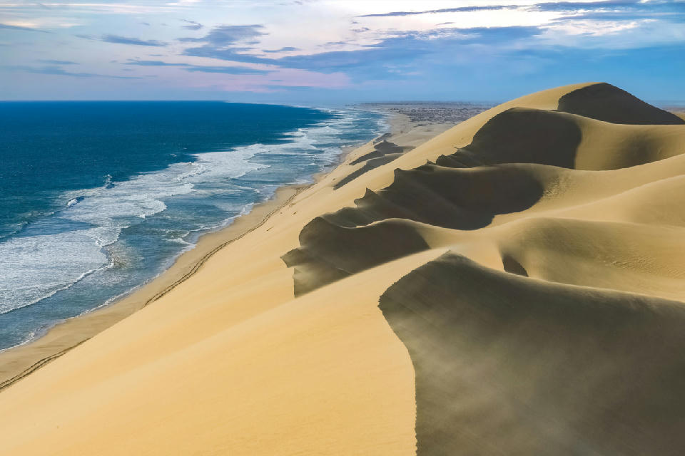 Sweeping aerial view of large sand dunes meeting the Atlantic Ocean along Namibia’s Skeleton Coast.