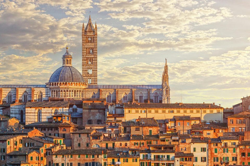 Sunset view of Siena rooftops with the dome and bell tower of Siena Cathedral in Siena, Tuscany, Italy.