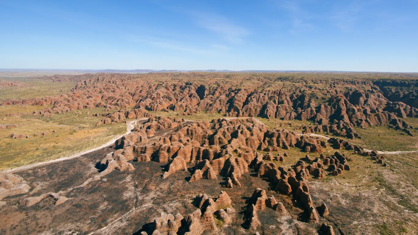 Sweeping aerial view across hundreds of orange-and-black striped sandstone domes and deep valleys of the Bungle Bungle Range.