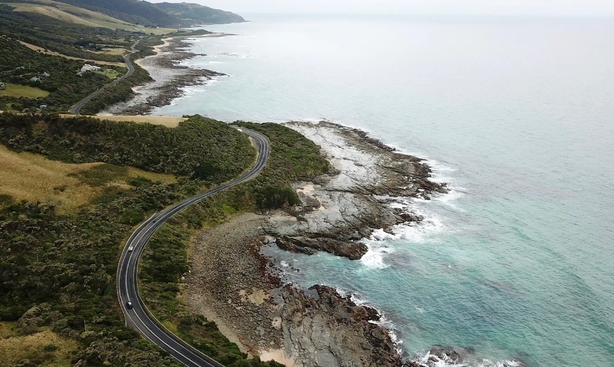 Aerial view of the Great Ocean Road curving beside rocky coastline and the Southern Ocean in Victoria, Australia.