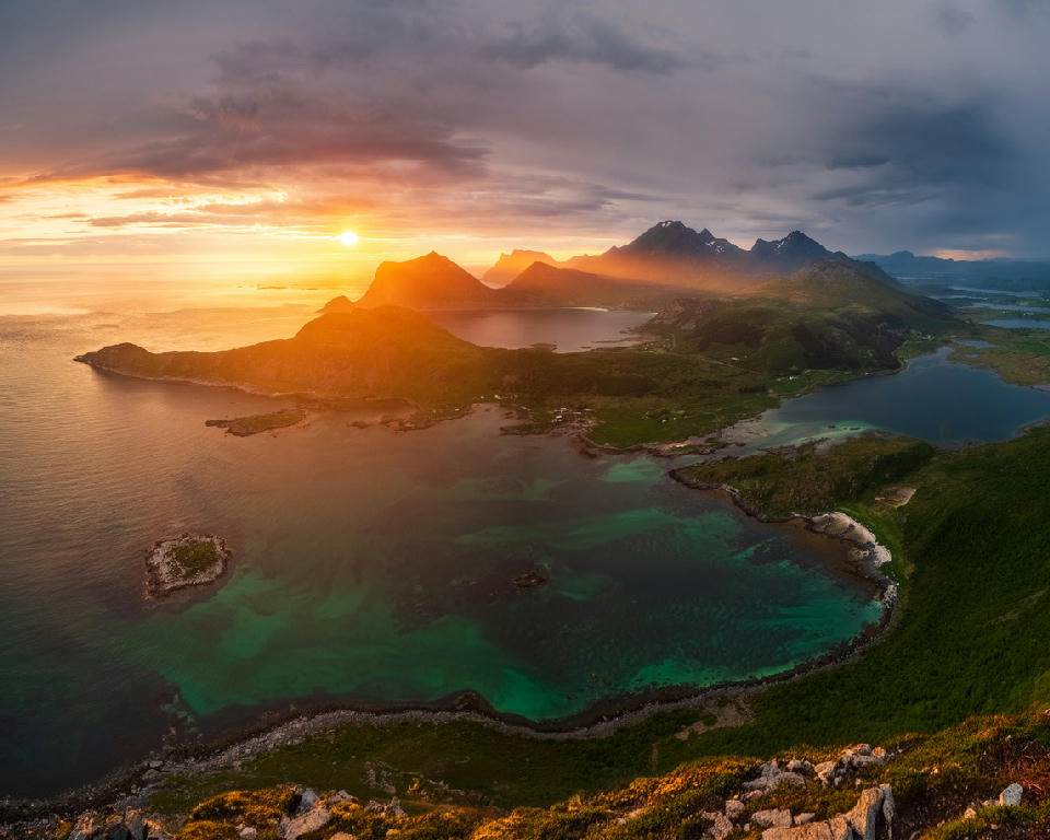 Sunset view from Offersøykammen on Vestvågøya in the Lofoten Islands, showing coastal lagoons, farmland and mountain silhouettes along the Norwegian Sea in Norway.