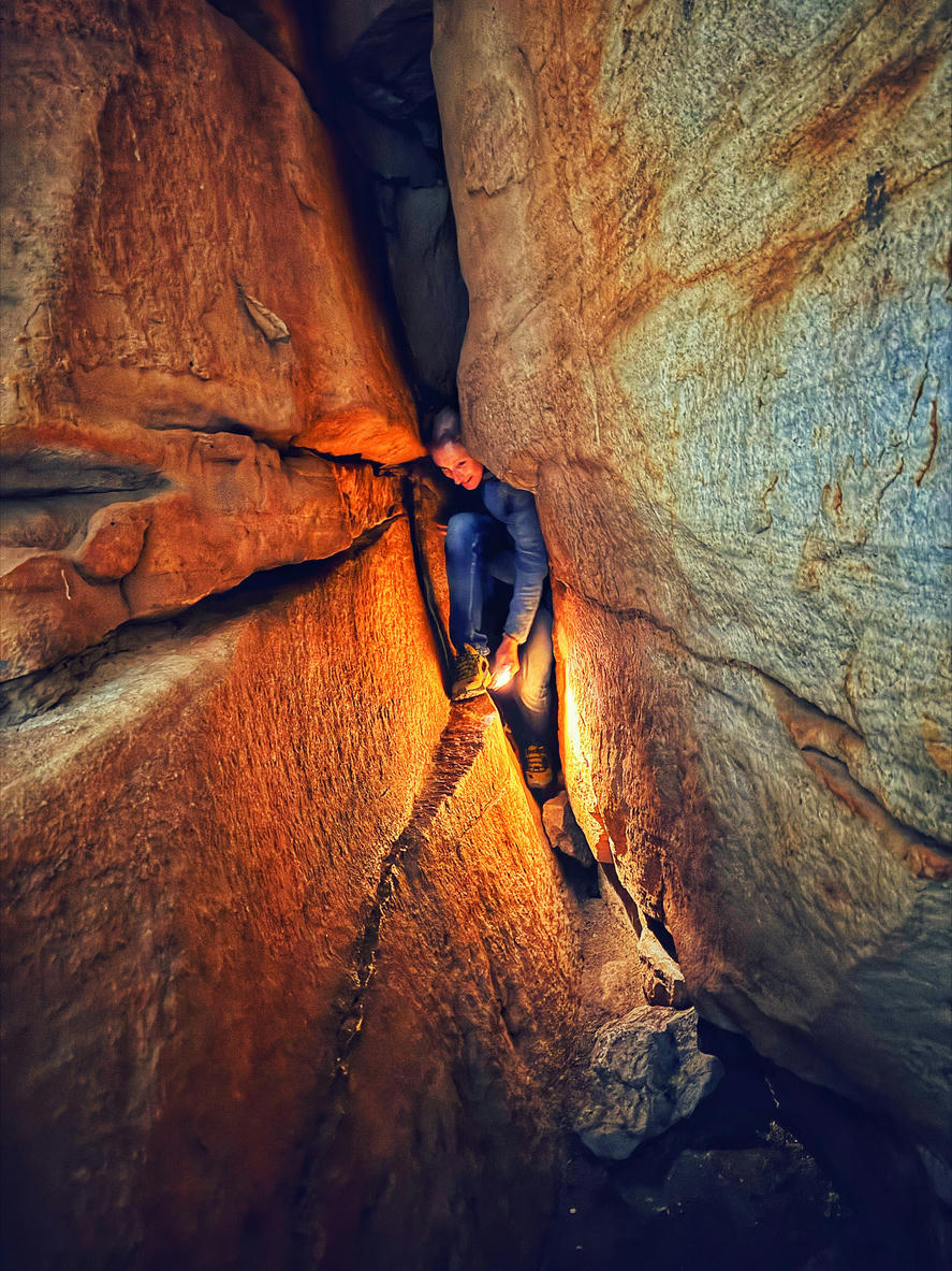 Hiker squeezing through a narrow sandstone passage inside Wolfberg Cracks in the Cederberg Wilderness Area, Western Cape, South Africa.