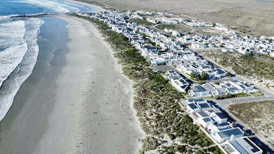 Aerial view of whitewashed houses and beachfront cottages lining the coastline at Paternoster on South Africa’s West Coast, with wide sandy beaches and Atlantic Ocean waves.