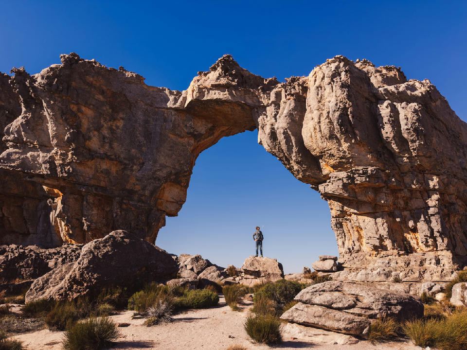 Wolfberg Arch sandstone formation in the Cederberg Wilderness with a hiker standing beneath the natural rock arch, Western Cape, South Africa.
