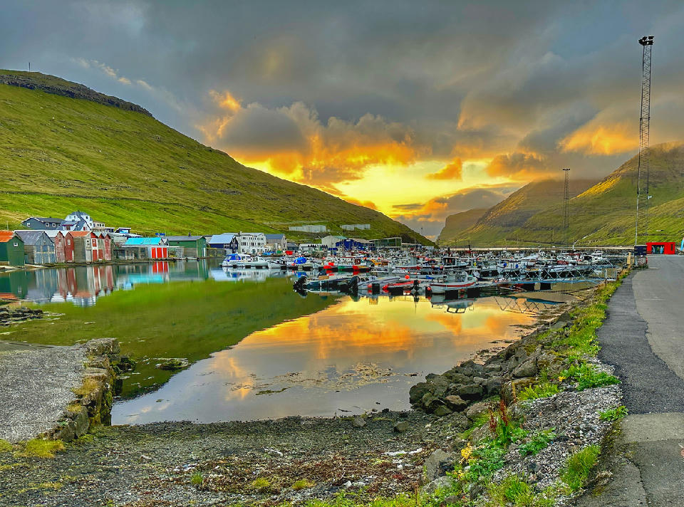 Fishing boats moored in the harbour of Sørvágur on Vágar Island, Faroe Islands, with mountains enclosing the fjord at sunset.