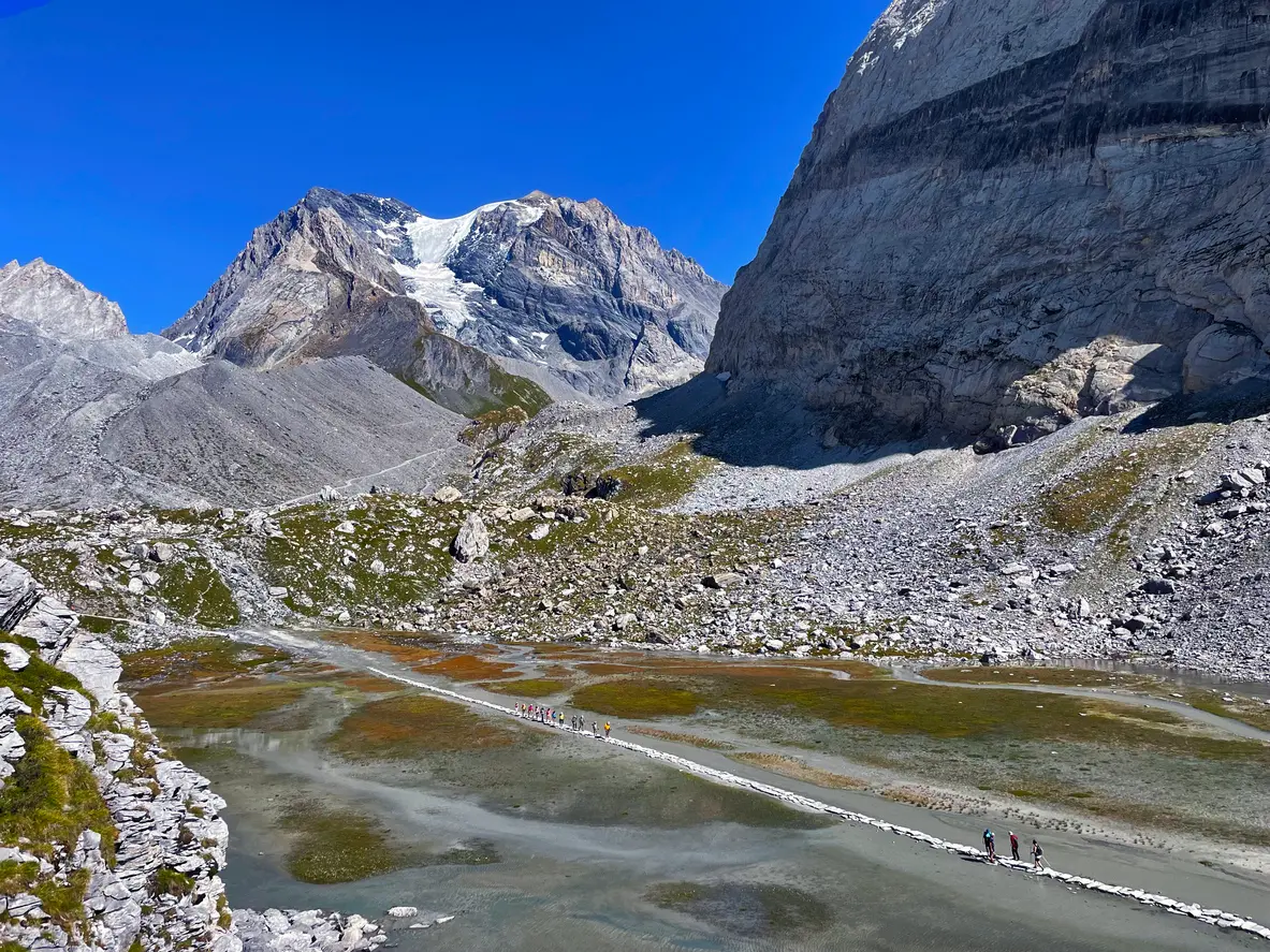 People crossing stepping stones at Lac des Vaches with alpine peaks and glacier in the background in Vanoise National Park