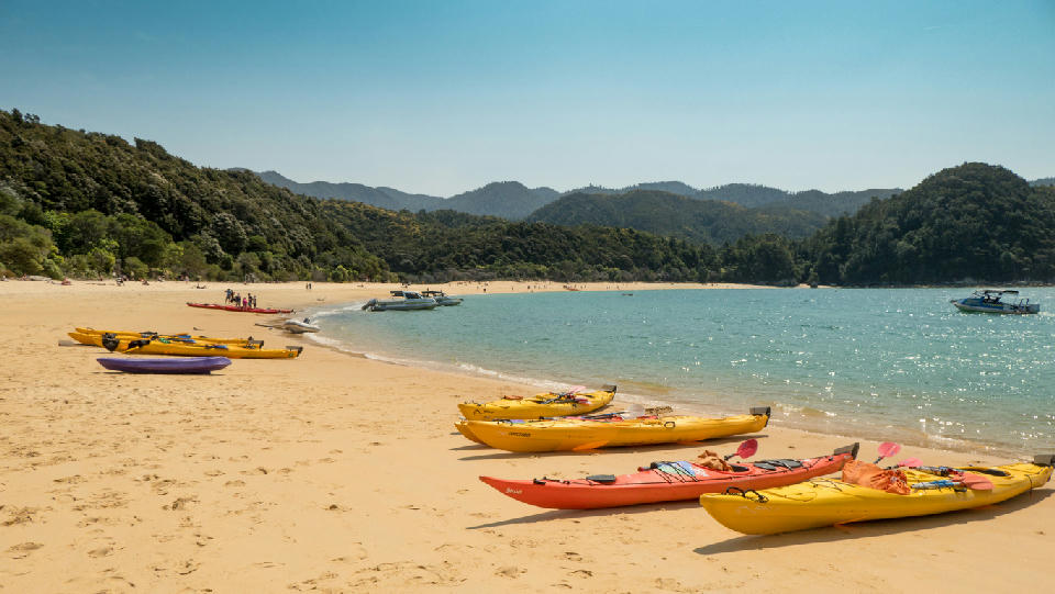 Sea kayaks resting on the golden sand of Anchorage Beach in Abel Tasman National Park, New Zealand.