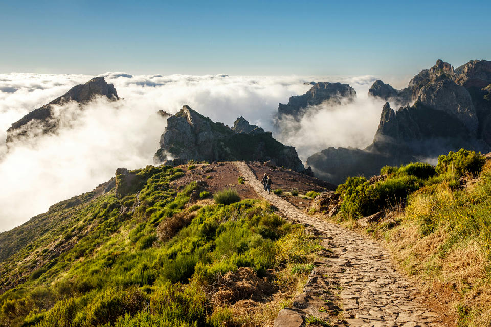 Mountain hiking trail near the summit of Pico do Arieiro, with stone path winding through rugged peaks above a sea of clouds.