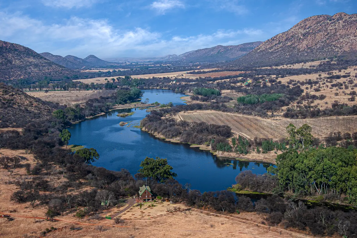 Aerial view of the Vaal River meandering through the Vredefort Dome landscape with hills, farmland and riverine vegetation in North West and Free State, South Africa.