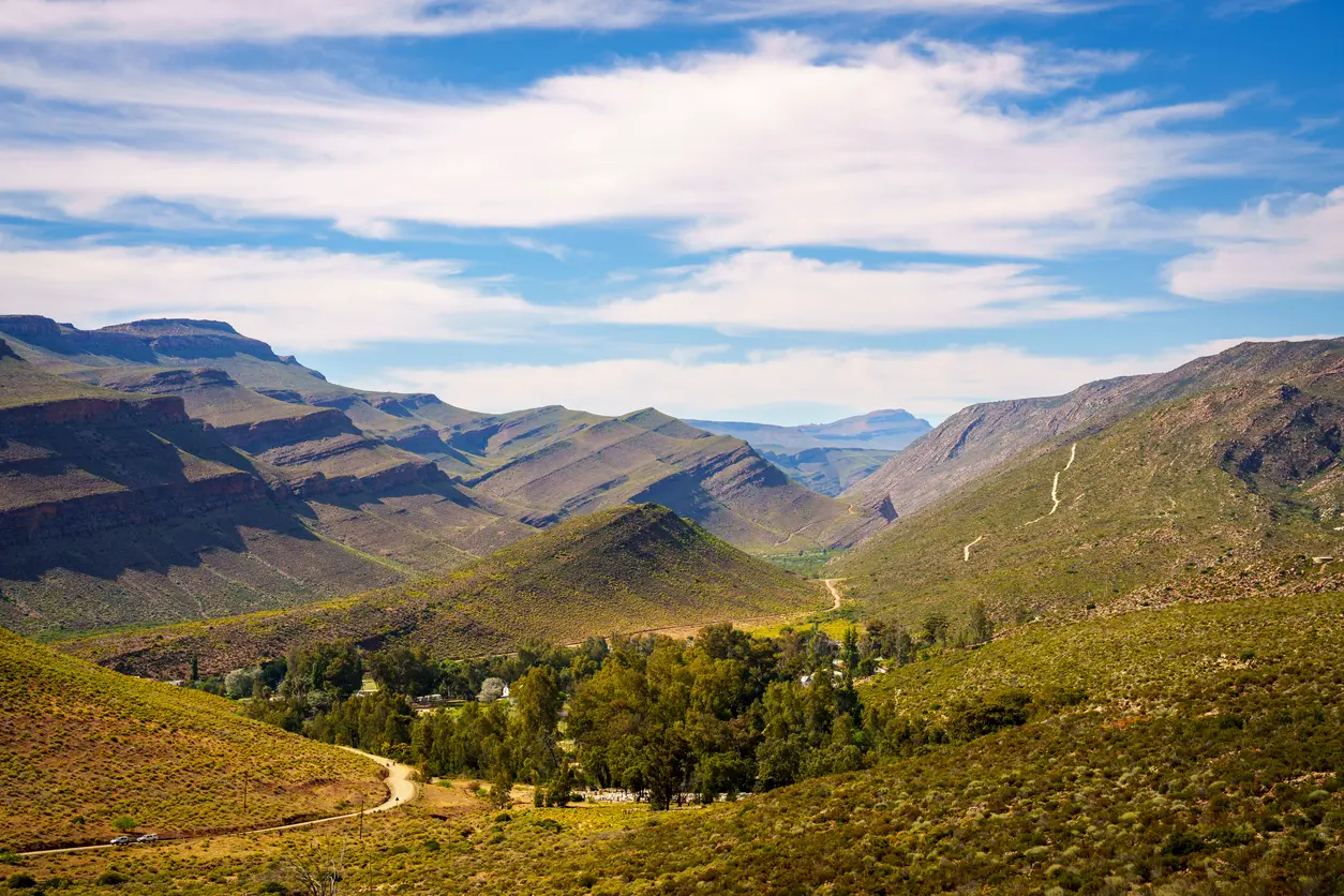 Wupperthal mission settlement nestled within the rugged Cederberg Mountains of South Africa, with winding roads, green valley vegetation, and layered sandstone ridges stretching into the distance.