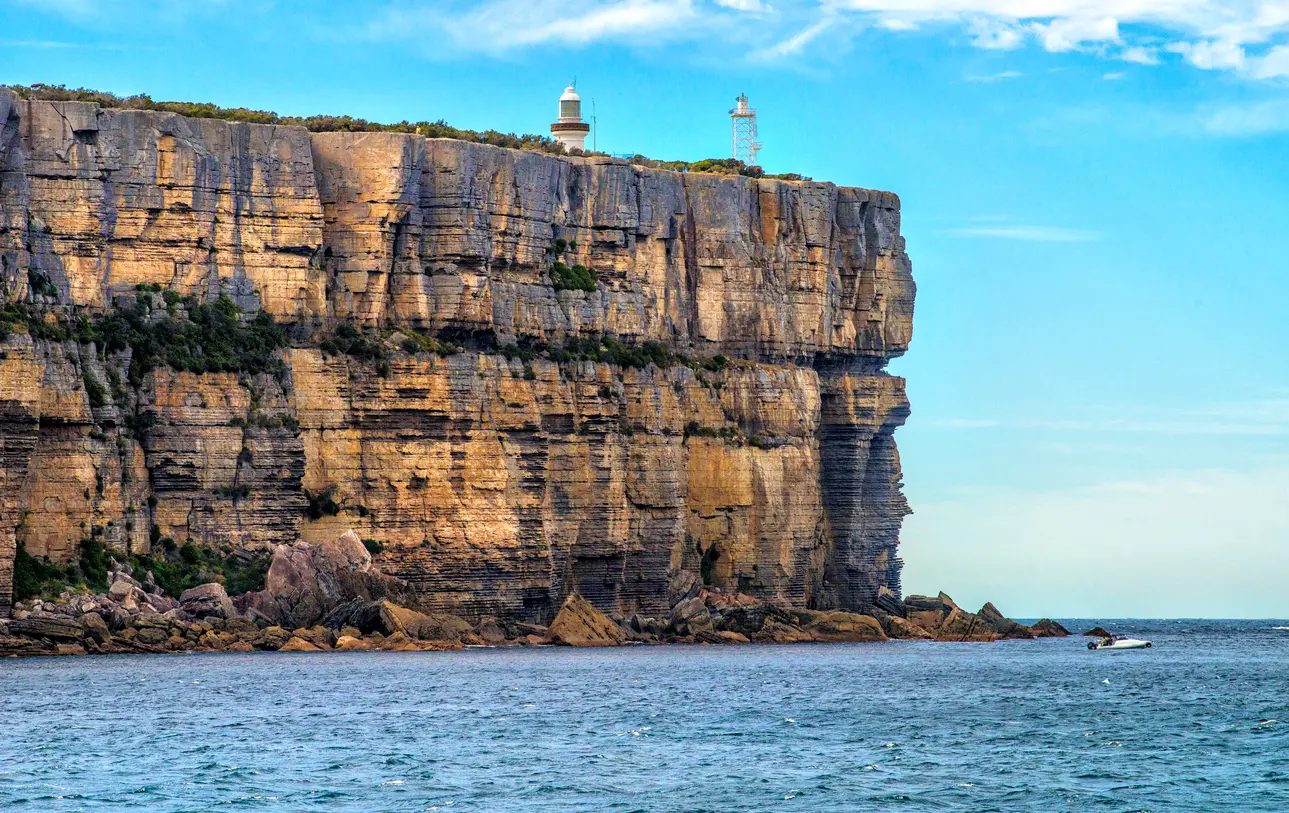 Point Perpendicular Lighthouse and navigation tower stand atop sheer layered sandstone cliffs rising above the ocean at the entrance to Jervis Bay.