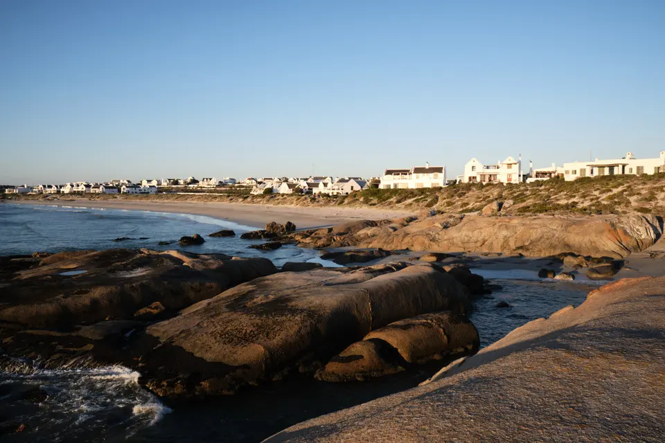 Granite shoreline, sandy beach and whitewashed coastal homes in Paternoster on South Africa's West Coast during golden-hour light.