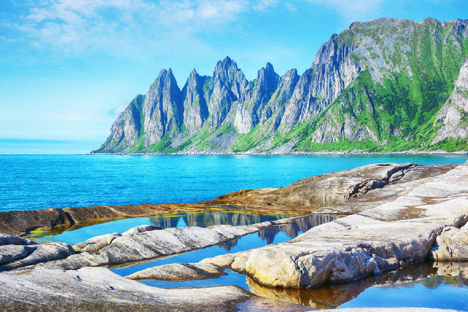 Jagged Okshornan peaks above Ersfjord with foreground tidal rock pools on Senja Island