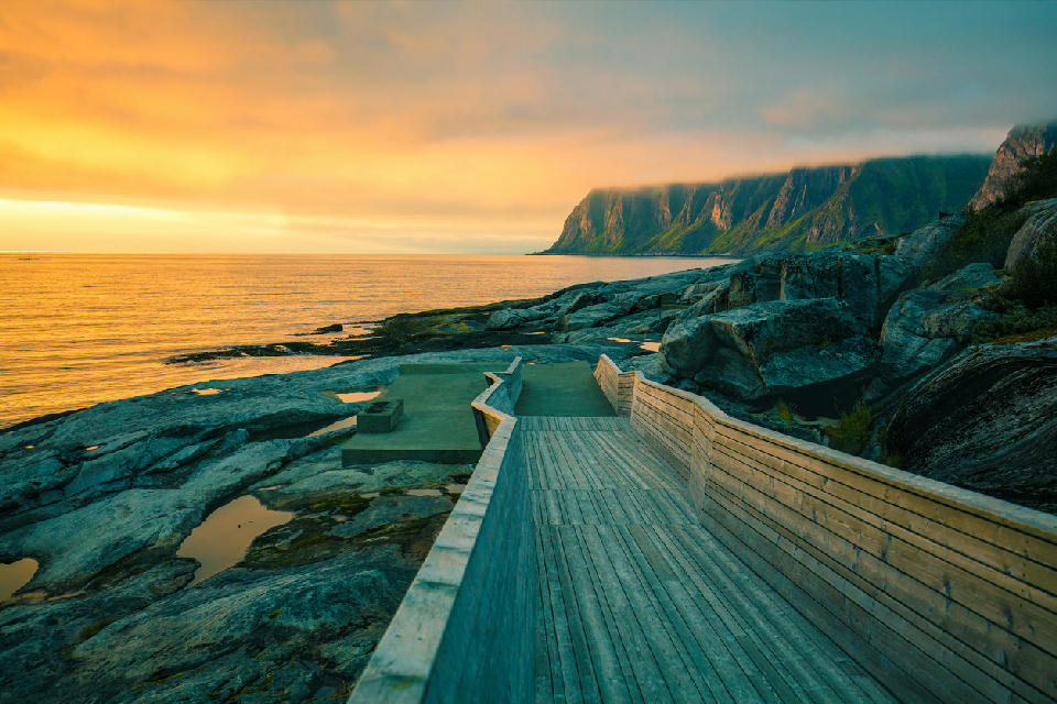 Tungeneset boardwalk on the outer coast of Senja, Norway, with wooden pathway leading across exposed rock toward the Okshornan (Devil’s Teeth) ridge.