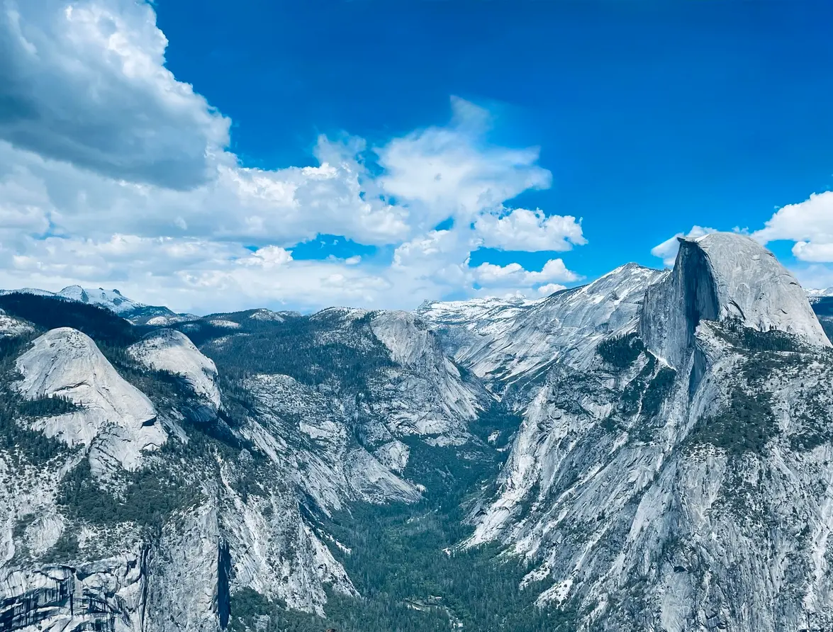 View from Glacier Point in Yosemite National Park showing Half Dome, granite cliffs, and Yosemite Valley beneath a blue sky with clouds.