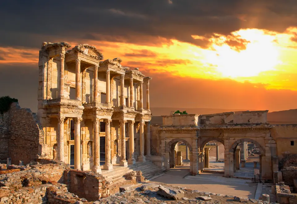 Library of Celsus and surrounding Roman ruins at Ephesus beneath a dramatic golden sunset sky.