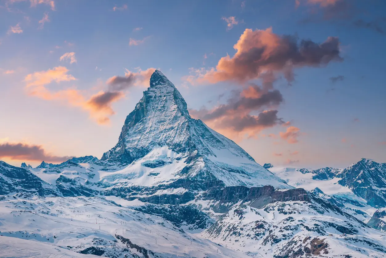 Matterhorn peak above Zermatt with snow-covered slopes and soft pink clouds at sunset, Swiss Alps