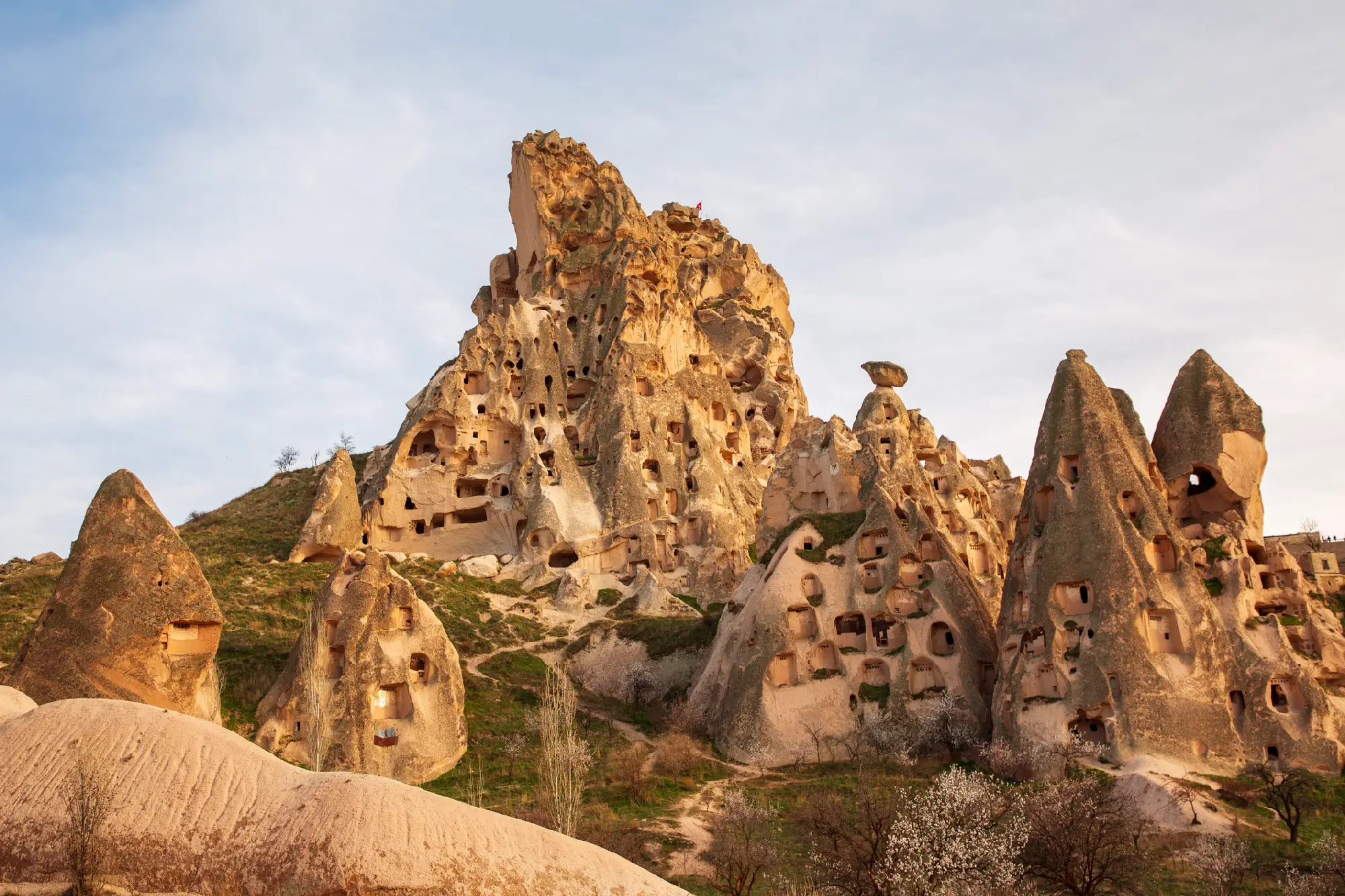 Uçhisar Castle surrounded by tall fairy chimneys and rock-cut cave dwellings in Cappadocia, Turkey.