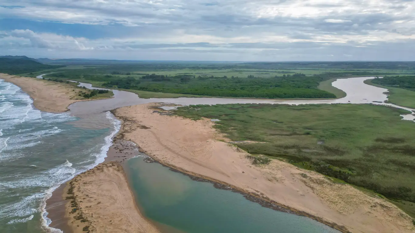 Aerial view of the St Lucia Estuary mouth in iSimangaliso Wetland Park, showing wetlands, sandbanks, winding channels and the Indian Ocean coastline in KwaZulu-Natal, South Africa.