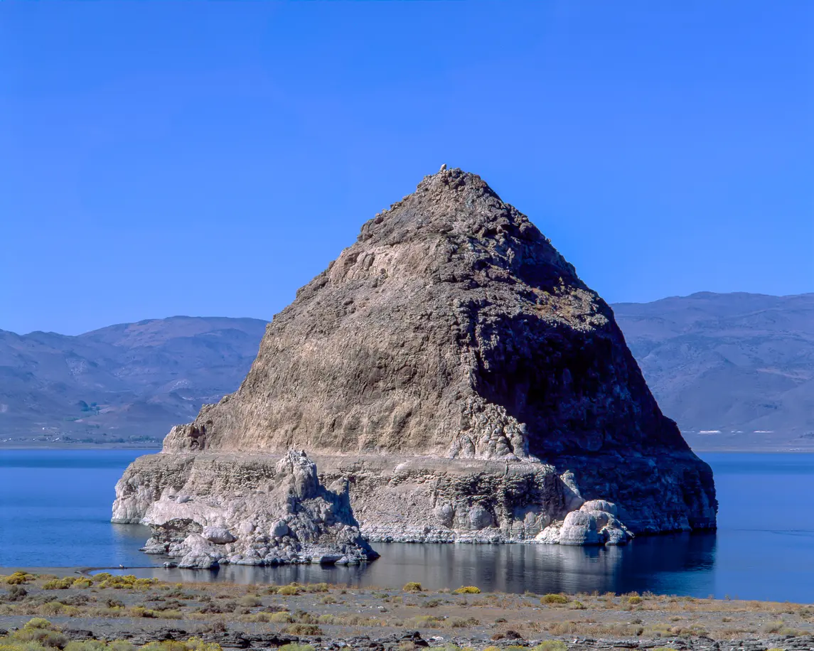 Triangular rock formation rising from Pyramid Lake with calm water and mountain backdrop