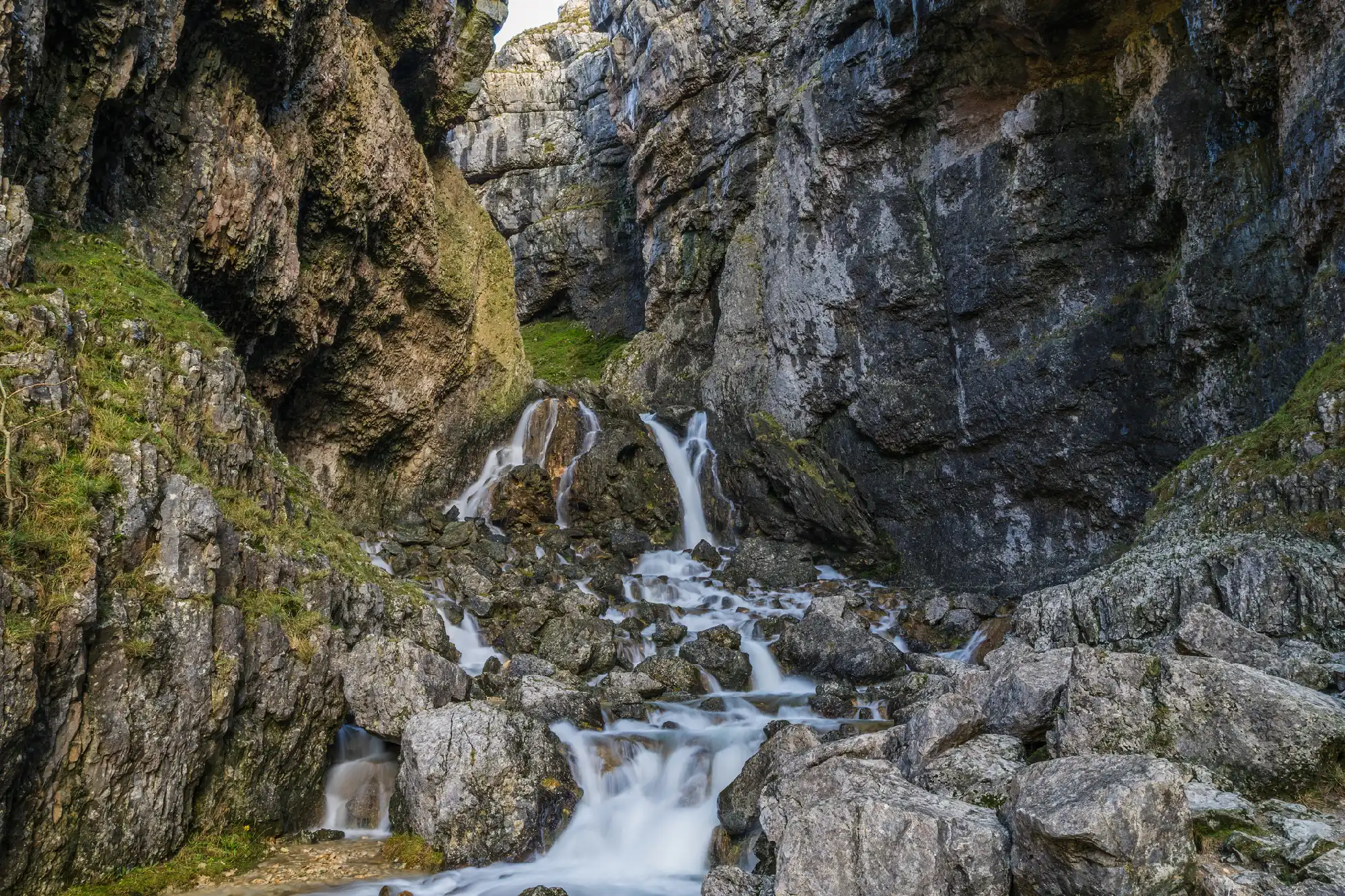 Cascading waterfalls flowing over limestone boulders between steep rock walls inside Gordale Scar, North Yorkshire.