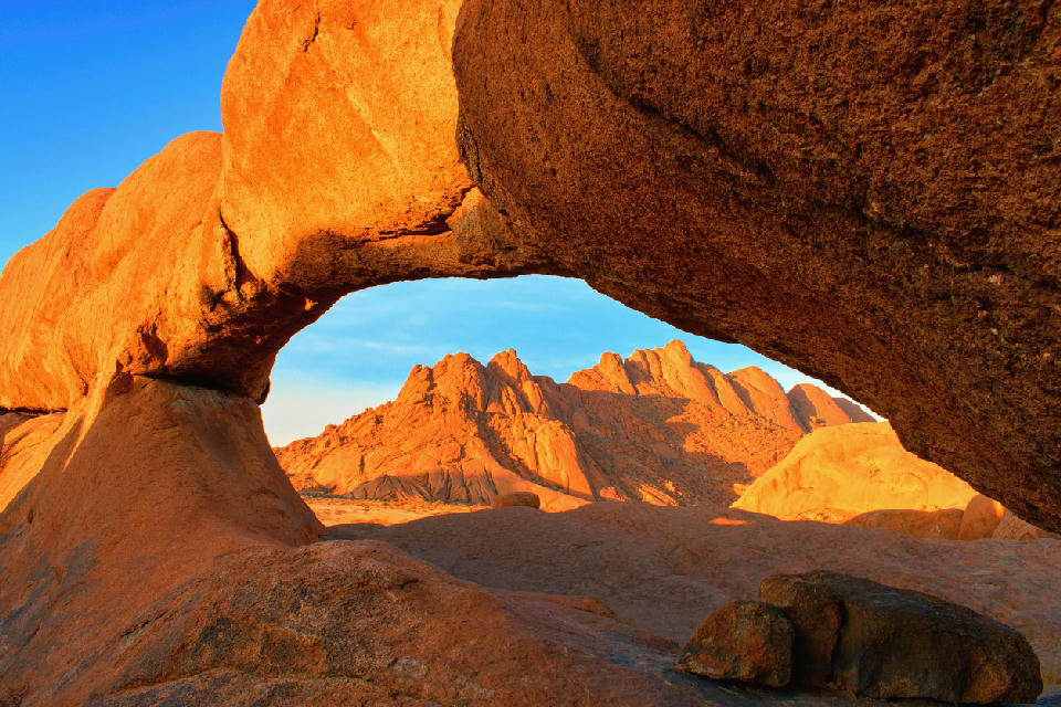 Granite rock arch at Spitzkoppe in Namibia framing sunlit desert peaks during golden hour.