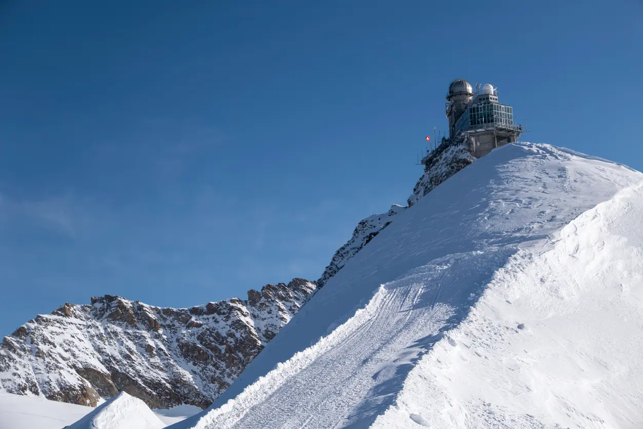 Sphinx Observatory at Jungfraujoch with snow ridge and alpine peaks under clear sky, Bernese Alps, Switzerland.