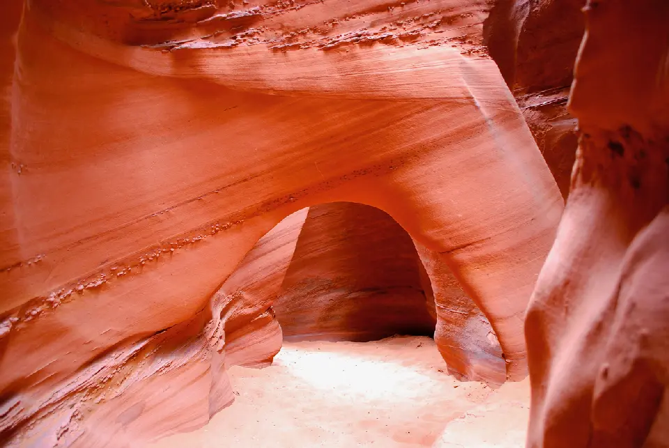 Smooth red sandstone walls form a natural arch above the narrow sandy passage through Peek-a-Boo Gulch slot canyon.