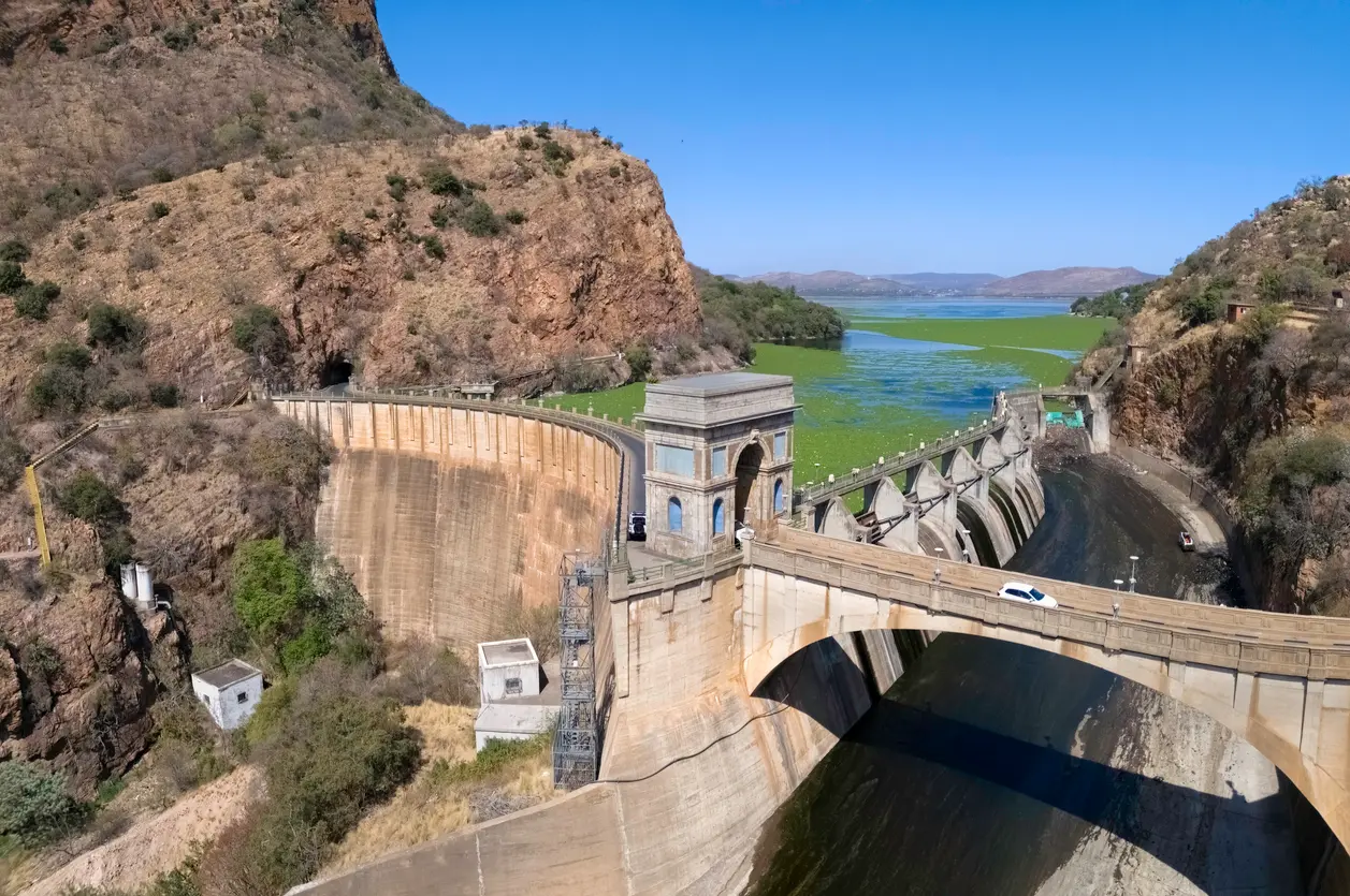 Aerial view of Hartbeespoort Dam and dam wall set between rocky Magaliesberg mountains, with the reservoir stretching into the distance in North West Province, South Africa.
