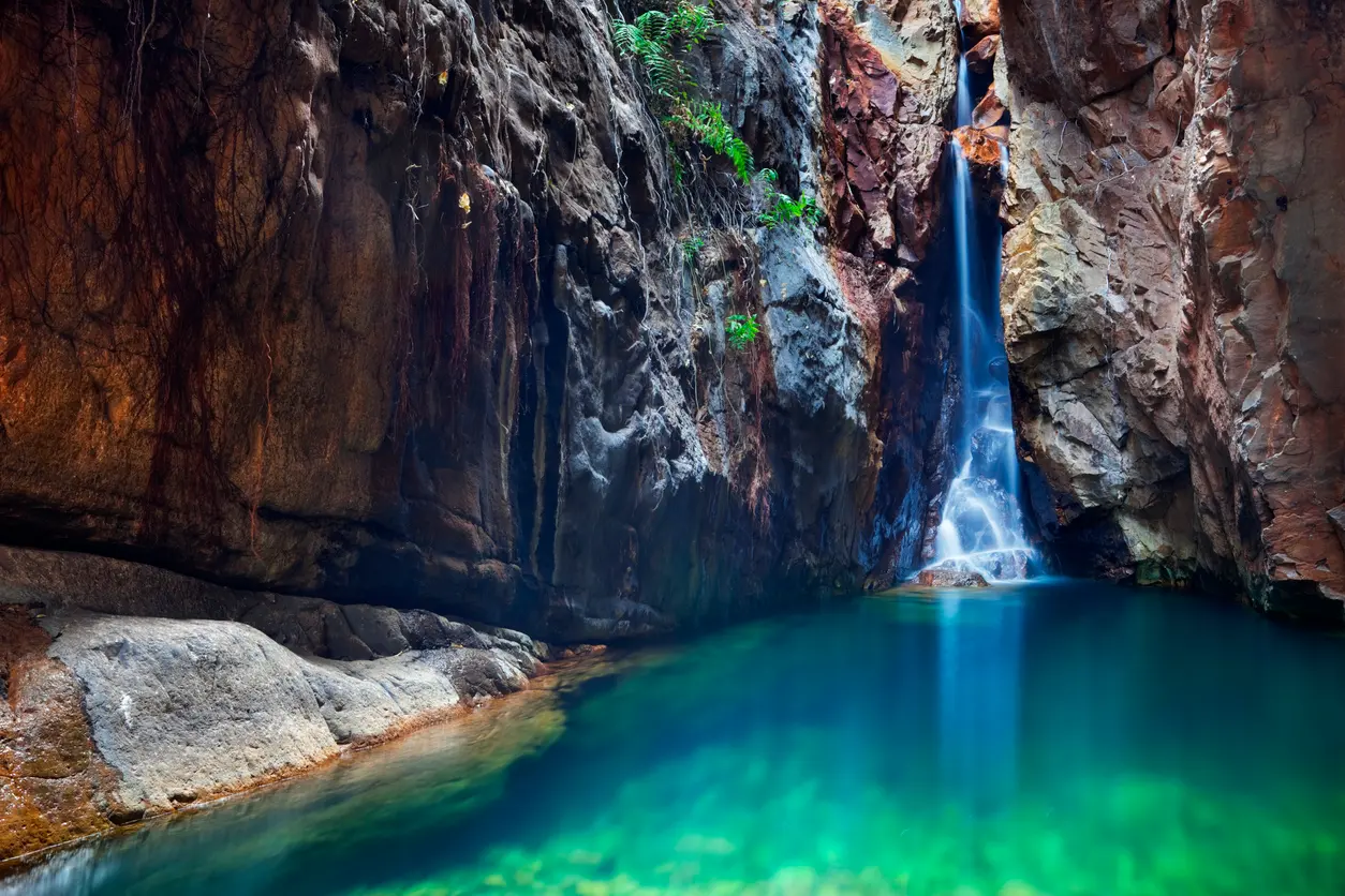Waterfall cascades between steep rock walls into a clear turquoise plunge pool in El Questro Gorge.