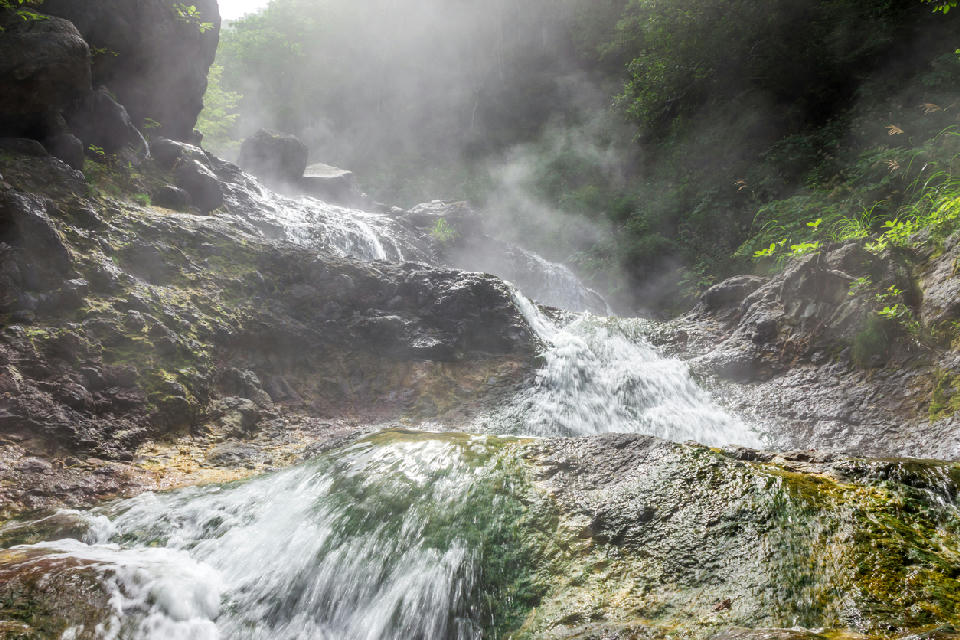 Steaming hot water cascading over mineral-stained rocks at Kamuiwakka Hot Falls in Shiretoko