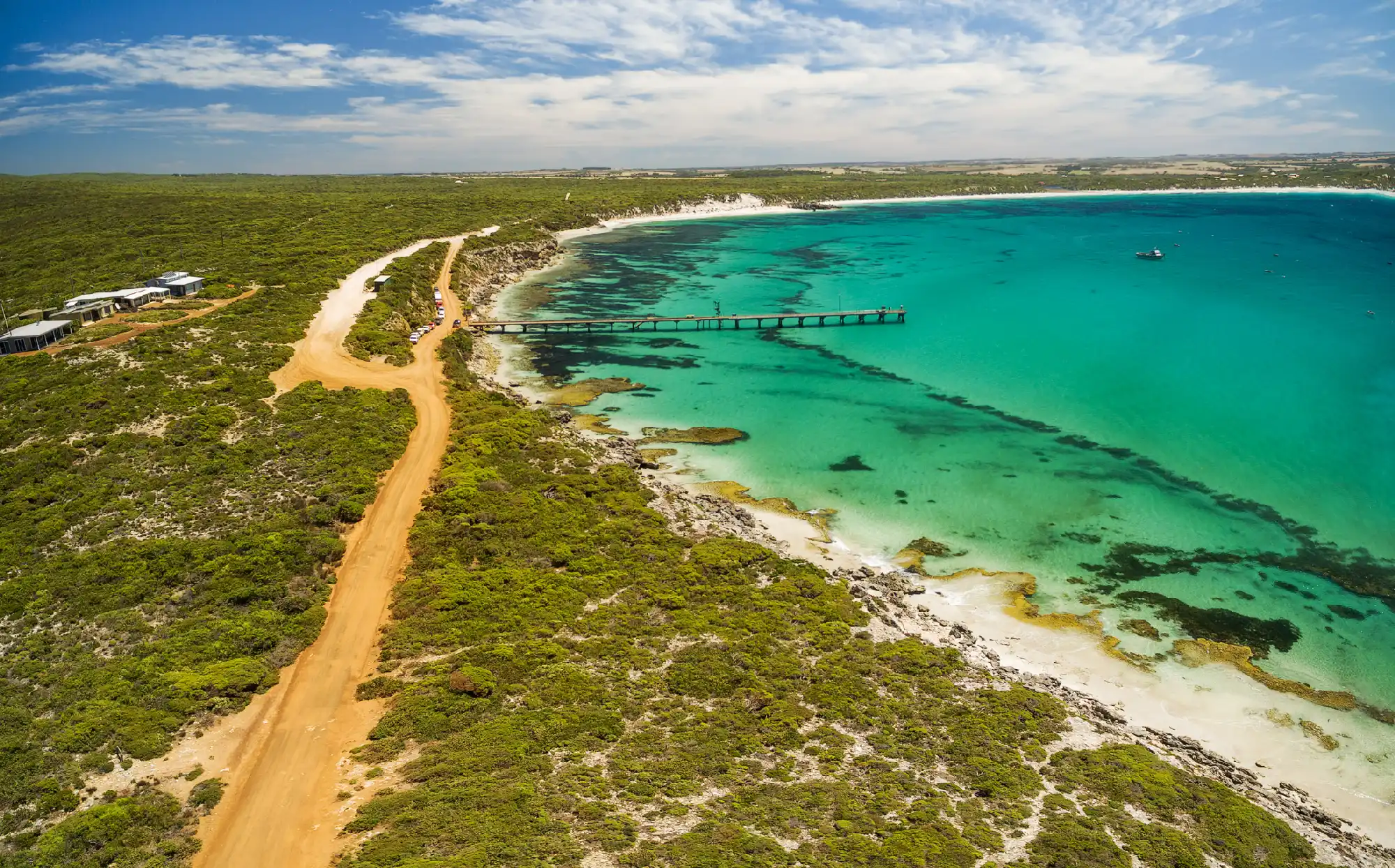 Aerial view of Vivonne Bay jetty, turquoise ocean water, white sandy beach and coastal access road on Kangaroo Island, South Australia.