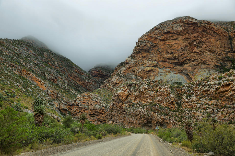 Gravel road winding beneath the folded sandstone cliffs of Seweweekspoort, one of the most dramatic mountain corridors in the Klein Karoo of South Africa.