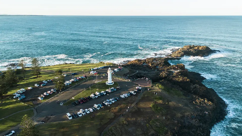 Aerial view of Kiama Lighthouse on Blowhole Point, surrounded by rugged volcanic rocks and the blue Pacific Ocean.